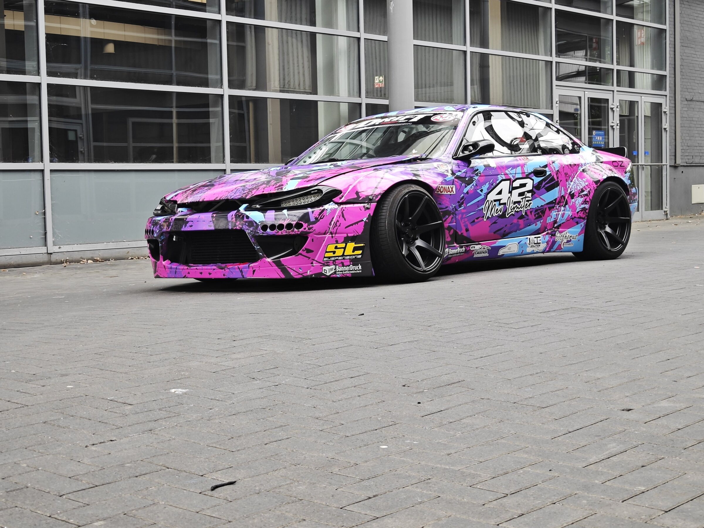 Nissan 200SX S14.9 „The Queen“ in Dreiviertel-Ansicht vor einer Glasfassade